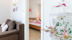 Une chambre d’hôtel moderne avec un canapé marron, un lit avec une literie à motifs floraux et une cage à oiseaux décorative blanche ornée de fleurs roses.