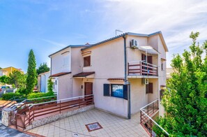 Ein zweigeschossiges Wohngebäude mit Balkon, gefliestem Patio und umlaufendem Grün.