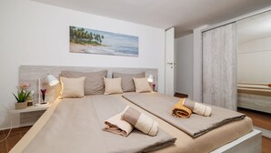Een tweepersoonsbed met twee kussens en een dekbed, een nachtkastje met een lamp, een kleine plant en een schilderij van een strandgezicht.