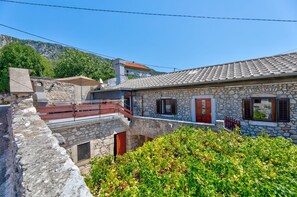 A stone house with a balcony, a stone wall, and a mountain backdrop.