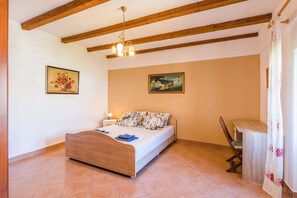 A bedroom with a wooden bed, two paintings, a bench, and a hanging light fixture.