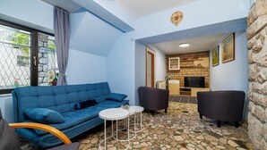 Een knusse woonkamer met een blauwe bank, twee fauteuils, een kleine witte tafel en een vloer met een stenen patroon.