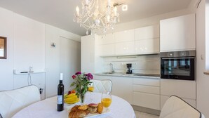 Una cocina moderna con armarios blancos, horno empotrado y comedor con una mesa redonda dispuesta para el desayuno.