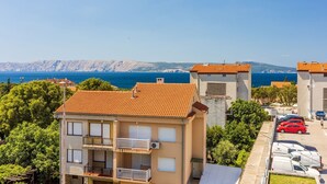 Un edificio costero con techo de tejas rojas, un balcón y vistas al mar y montañas al fondo.