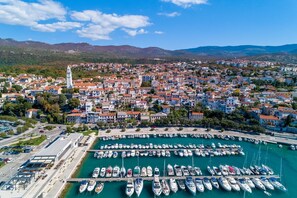 An aerial view of a coastal town with a marina filled with boats, surrounded by residential buildings and a prominent church tower. - Modern studio apartment just 100 metres from the beach with stunning sea views (Novi Vinodolski)