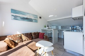 A modern living room with a sofa, a small white table, and a kitchen area with a refrigerator and microwave. - Modern studio apartment just 100 metres from the beach with stunning sea views (Novi Vinodolski)