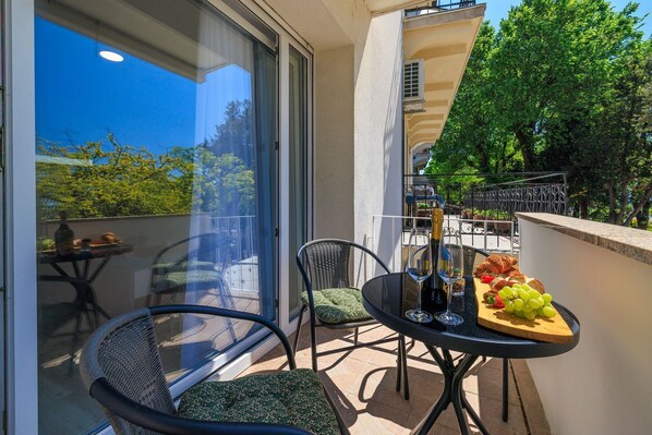 A balcony with a table set for two, featuring a bottle of wine, glasses, and a fruit platter. - Fantastic apartment right on the beach promenade with lots of palm trees (Crikvenica)