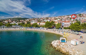 Uma cidade costeira com uma praia, águas cristalinas e edifícios ao fundo.