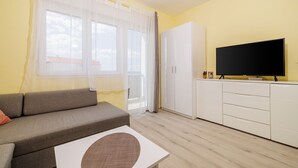 Un soggiorno con un divano, una televisione su un mobile e una finestra con tende.