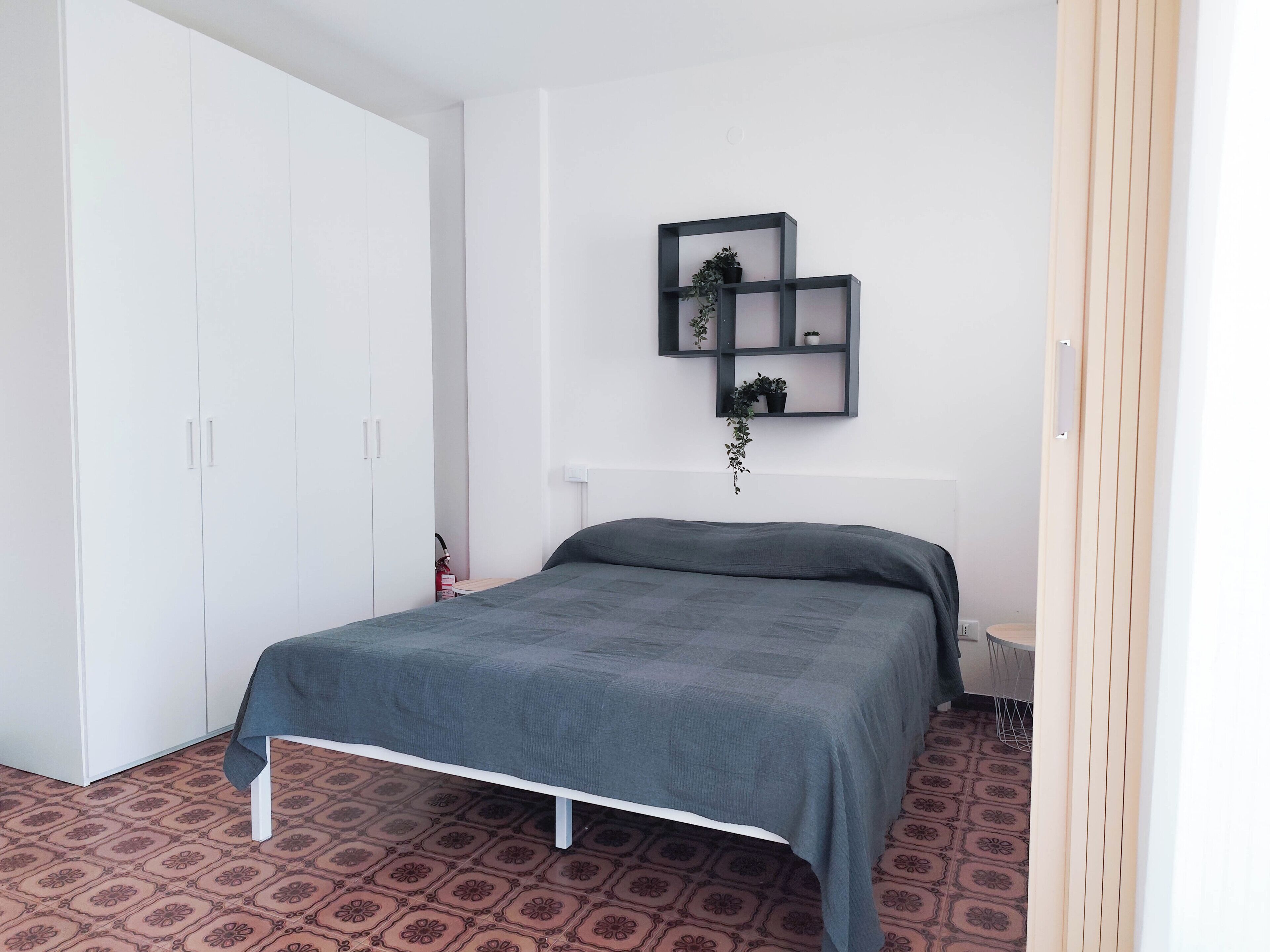 Une chambre à coucher avec un lit, une armoire et une étagère murale agrémentée de plantes.