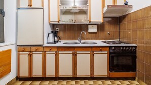 Una cocina pequeña con armarios de madera, estufa, pileta y cafetera.