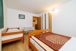 Ein Zimmer mit zwei Holzbetten, einem kleinen Tisch mit Tischdecke und einer Tür zu einem Badezimmer.