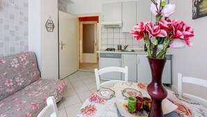 Een woonkamer met een bloemenbank, een eettafel met een bloevas, en een keuken op de achtergrond.