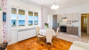 A modern kitchen with a view of the sea, a dining area with a table and chairs, and a cozy living space with a sofa. - Bright apartment just 200 metres from the sandy beach with sea views (Crikvenica)