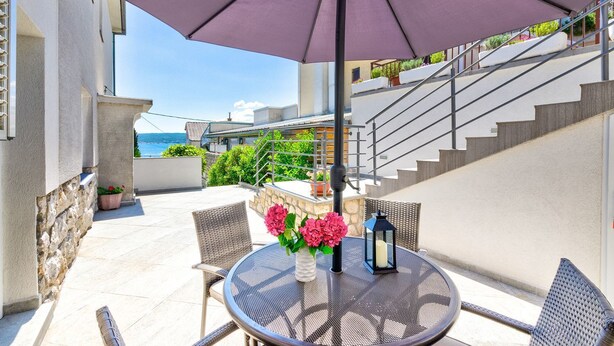Une terrasse avec une table ronde, des chaises, un parasol violet et des plantes en pot.