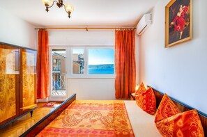 Ein Schlafzimmer mit einem großen Bett, orangefarbenen Vorhängen, Meerblick und einem Bild an der Wand.