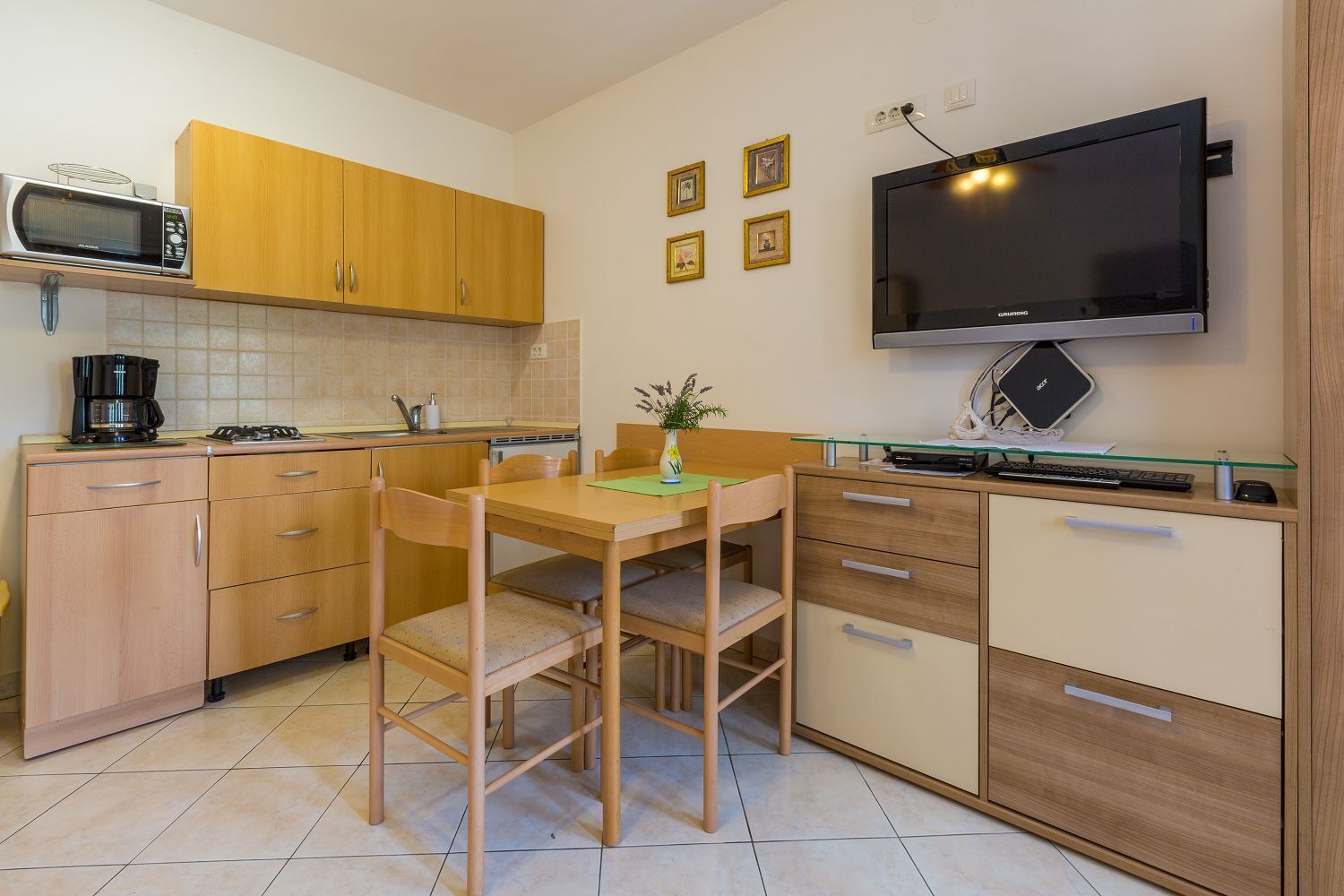 Een compacte keuken met houten kastjes, een magnetron, een koffiezetapparaat en een televisie op een standaard.