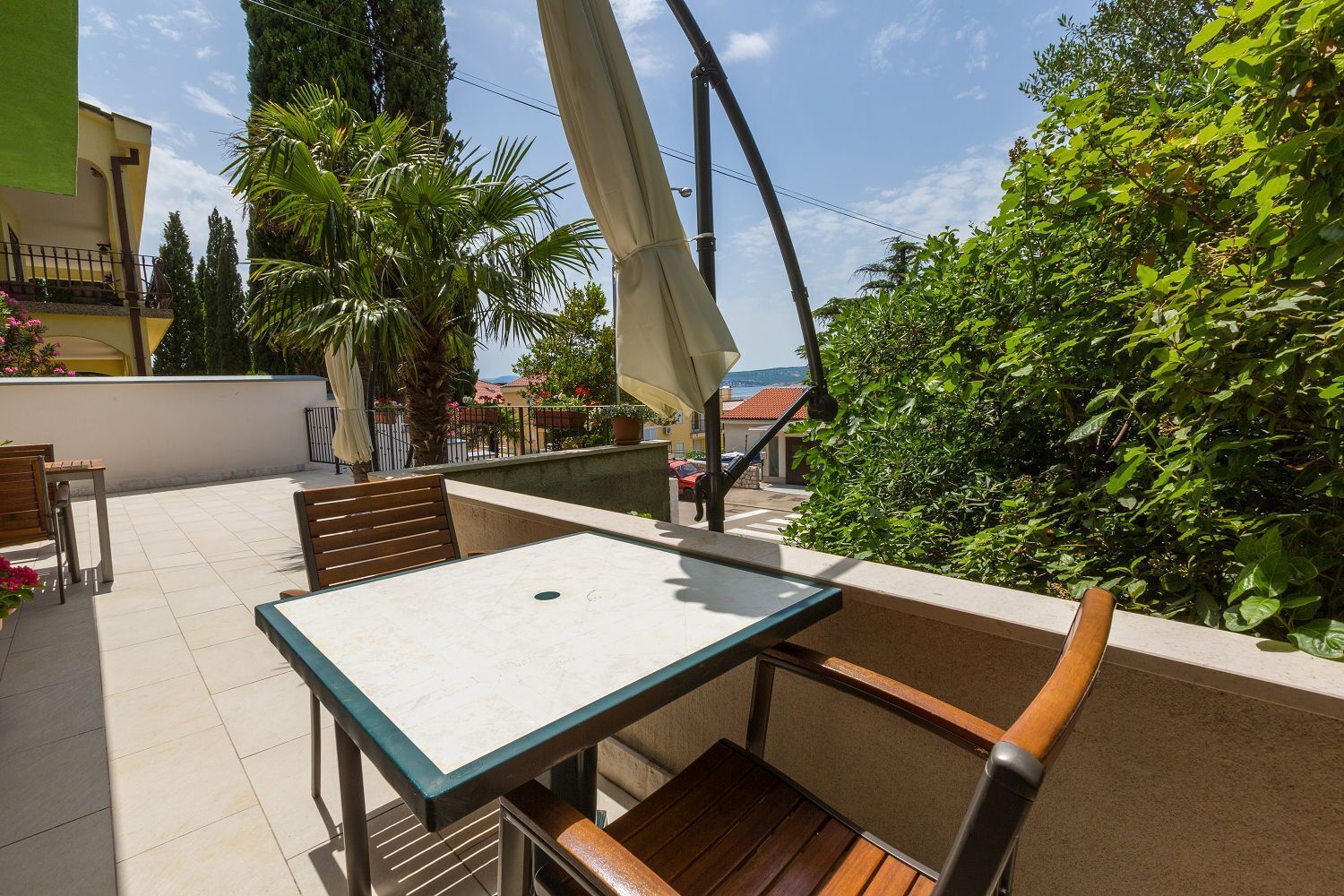 Patio esterno con tavolo e sedie, immerso nel verde e vista mare.