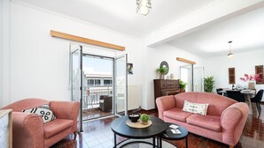 Uma sala de estar ampla com dois sofás cor-de-rosa, uma mesa de centro redonda e um espaço de refeições com mesa e cadeiras.