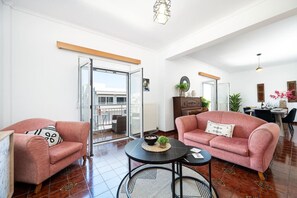 A spacious living room with two pink sofas, a round coffee table, and a dining area with a table and chairs. - Massive 4BR Retro Apartment | 3 min Walk to Beach (Kos)