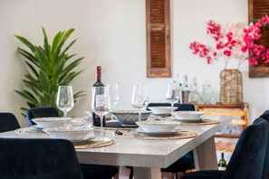 A dining table set with plates, glasses, and a bottle of wine, surrounded by chairs. - Massive 4BR Retro Apartment | 3 min Walk to Beach (Kos)