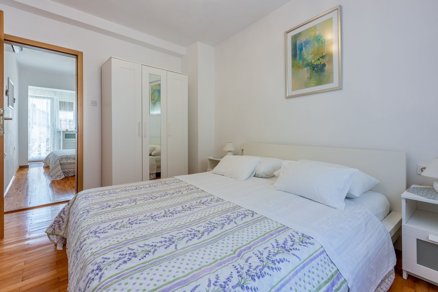 Een slaapkamer met een groot bed, een kledingkast, een nachtkastje en een schilderij aan de muur.