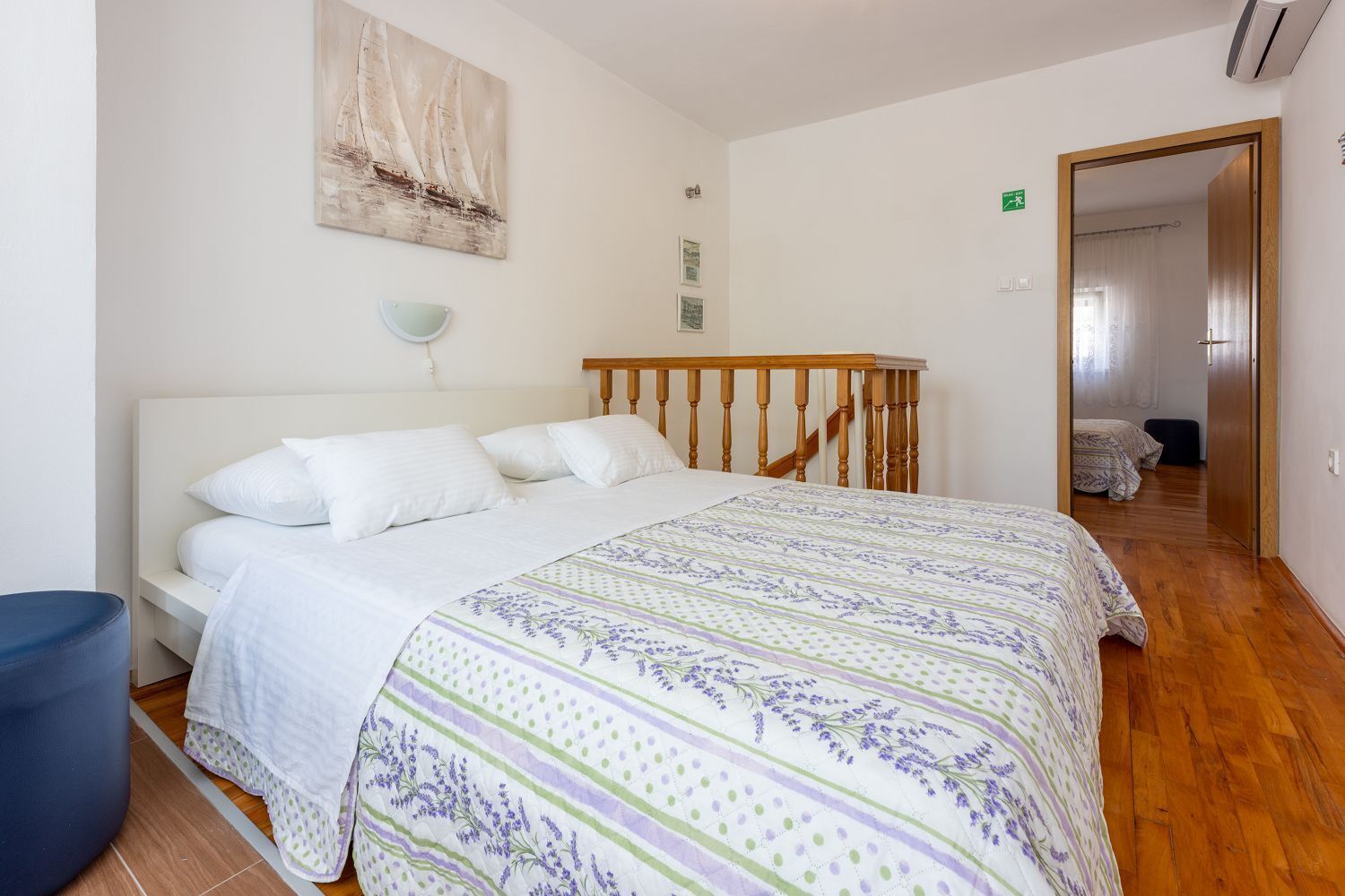 Een slaapkamer met een bed, nachtkastje, lamp en een schilderij aan de muur.