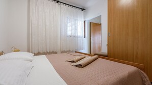 Un letto rifatto con cura, con una coperta rosa, cuscini bianchi e un asciugamano arrotolato.