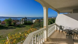 Un balcone con vista sul mare e sugli edifici, un tavolo con sedie e una ringhiera.