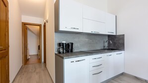 Ett modernt kök med vita skåp, en grå bänkskiva och en kaffebryggare.