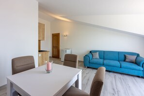 Ein modernes Wohnzimmer mit einem blauen Sofa, einem weißen Tisch und einer Küche im Hintergrund.