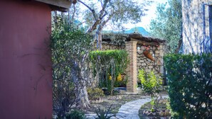 A stone building with a thatched roof, surrounded by lush greenery and a stone pathway. - Valory’s Stone Tower (Ano Vasilikos)