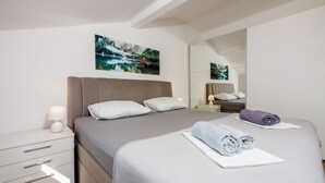 Quarto de hotel moderno com uma cama grande, mesa de cabeceira, luminária, espelho e uma pintura de paisagem de montanhas.