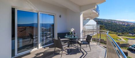 A balcony with a table and chairs, large sliding glass doors, and a view of a distant landscape.