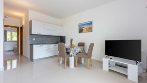A modern kitchen with white cabinets, a dining table with four chairs, and a flat-screen TV on a white stand. - Fascinating apartment with barbecue area, sea view, parking space, washing machine (Crikvenica)