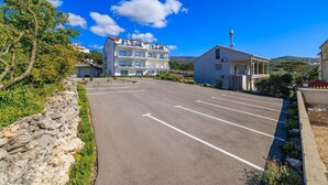 A parking lot with a row of buildings in the background, including a multi-story hotel with balconies and a smaller single-story building. - Fascinating apartment with barbecue area, sea view, parking space, washing machine (Crikvenica)