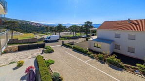 A parking area with a white van, a building with a red-tiled roof, and a view of a coastal landscape. - Fascinating apartment with barbecue area, sea view, parking space, washing machine (Crikvenica)
