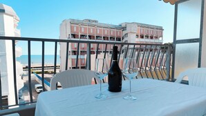A balcony with a table set for two, a bottle of wine, and two wine glasses. - Beachside Studio With Shared Pool (Jesolo)
