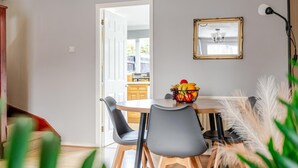 Un comedor con una mesa redonda, dos sillas, un frutero y un espejo en la pared.
