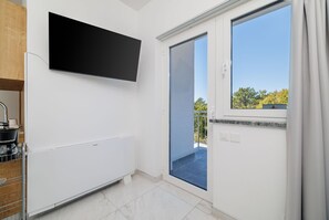 A modern kitchen with a built-in stove, a flat-screen TV, and a sliding glass door leading to a balcony. - Unique studio apartment with picturesque sea views (Crikvenica)
