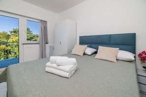 A neatly made bed with a patterned bedspread, a stack of white towels, and a blue headboard. - Unique studio apartment with picturesque sea views (Crikvenica)