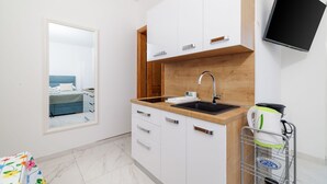 Una cocina moderna con armarios blancos, encimera de madera, pileta negra y televisor integrado.