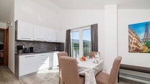 A modern kitchen with white cabinets and a dining area with a table set for two. - Stunning apartment with great sea views, washing machine, barbecue area (Crikvenica)