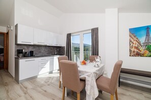 A modern kitchen with white cabinets and a dining area with a table set for two. - Stunning apartment with great sea views, washing machine, barbecue area (Crikvenica)