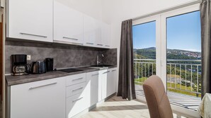 A modern kitchen with white cabinets, a grey countertop, and a coffee maker. There is a balcony with a view of a green landscape and buildings. - Stunning apartment with great sea views, washing machine, barbecue area (Crikvenica)