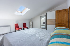 A bedroom with a skylight, a bed with a striped blanket, a red chair, and a wooden door. - Picturesque apartment with magnificent sea views, barbecue area, washing machine (Crikvenica)