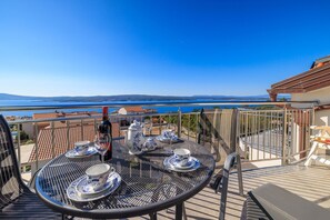 A balcony with a table set for tea, a bottle of wine, and a view of the sea and hills. - Picturesque apartment with magnificent sea views, barbecue area, washing machine (Crikvenica)