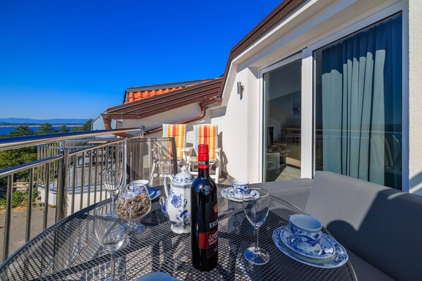 A table set for two with a bottle of wine, glasses, and blue and white dinnerware on a balcony overlooking a scenic view. - Picturesque apartment with magnificent sea views, barbecue area, washing machine (Crikvenica)