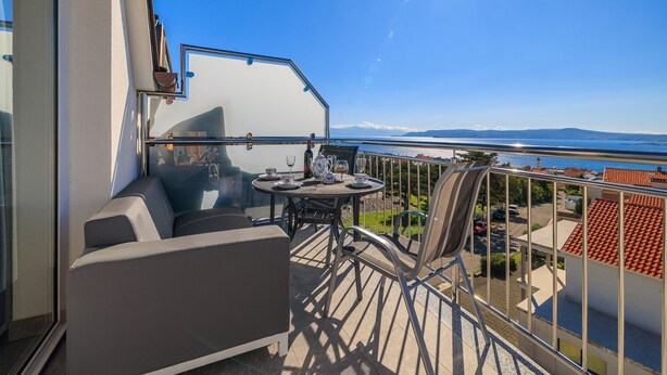 Un balcon avec une table et des chaises, un canapé et une vue sur la mer et les montagnes.