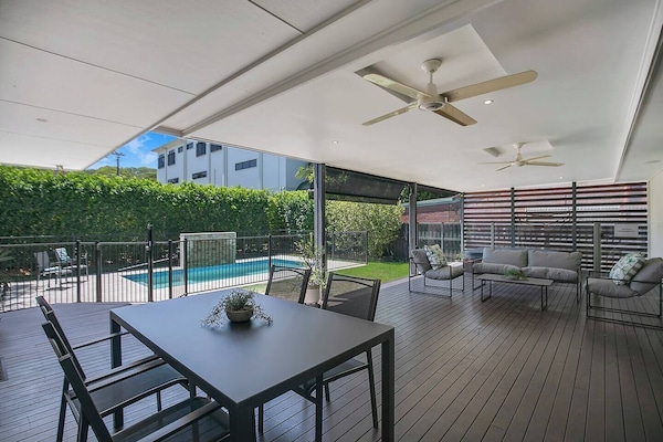 A spacious, covered deck designed for easy alfresco living, with a comfortable lounge and dining setting beneath ceiling fans, overlooking the private backyard and pool for relaxed meals, shaded downtime, and long afternoons outdoors.